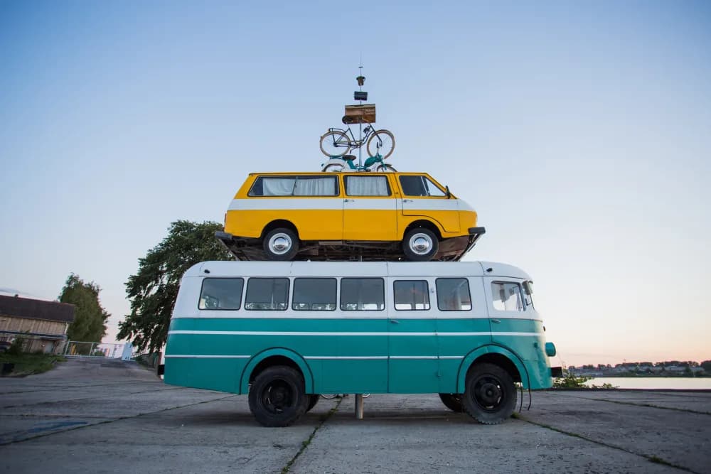 A totem pole of busses and bicycles. A blue 70s-era bus on the bottom, a yellow 60s-era bus on top of that and two bicycles to round out the top.