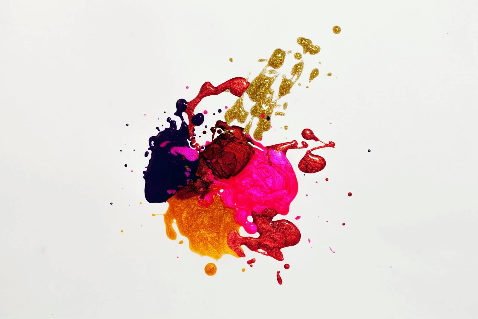 A splash of paint, including pink, gold, red, blue, and yellow, on a white canvas.