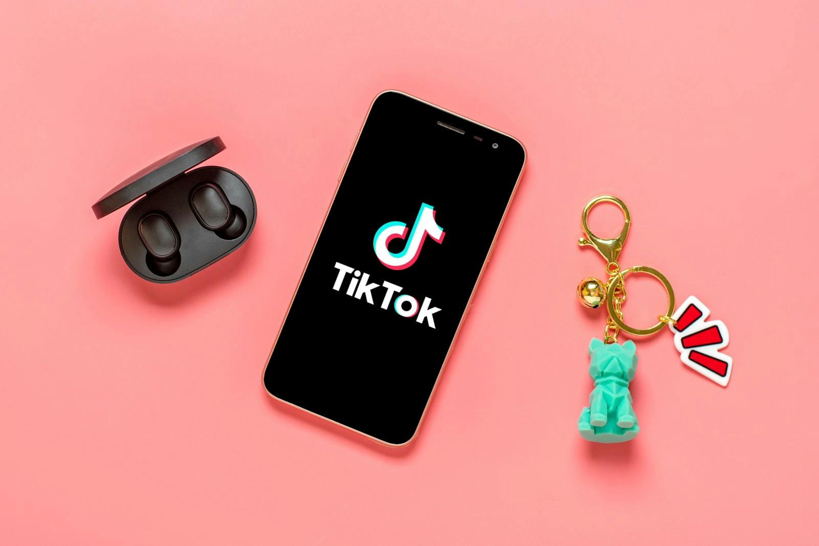 Headphones to the left, a mobile device in the middle, and a funky keychain with golden house keys on the right, all over a salmon background to highlight how TikTok is just one of the many ways consumers listen to your music today, in 2022.