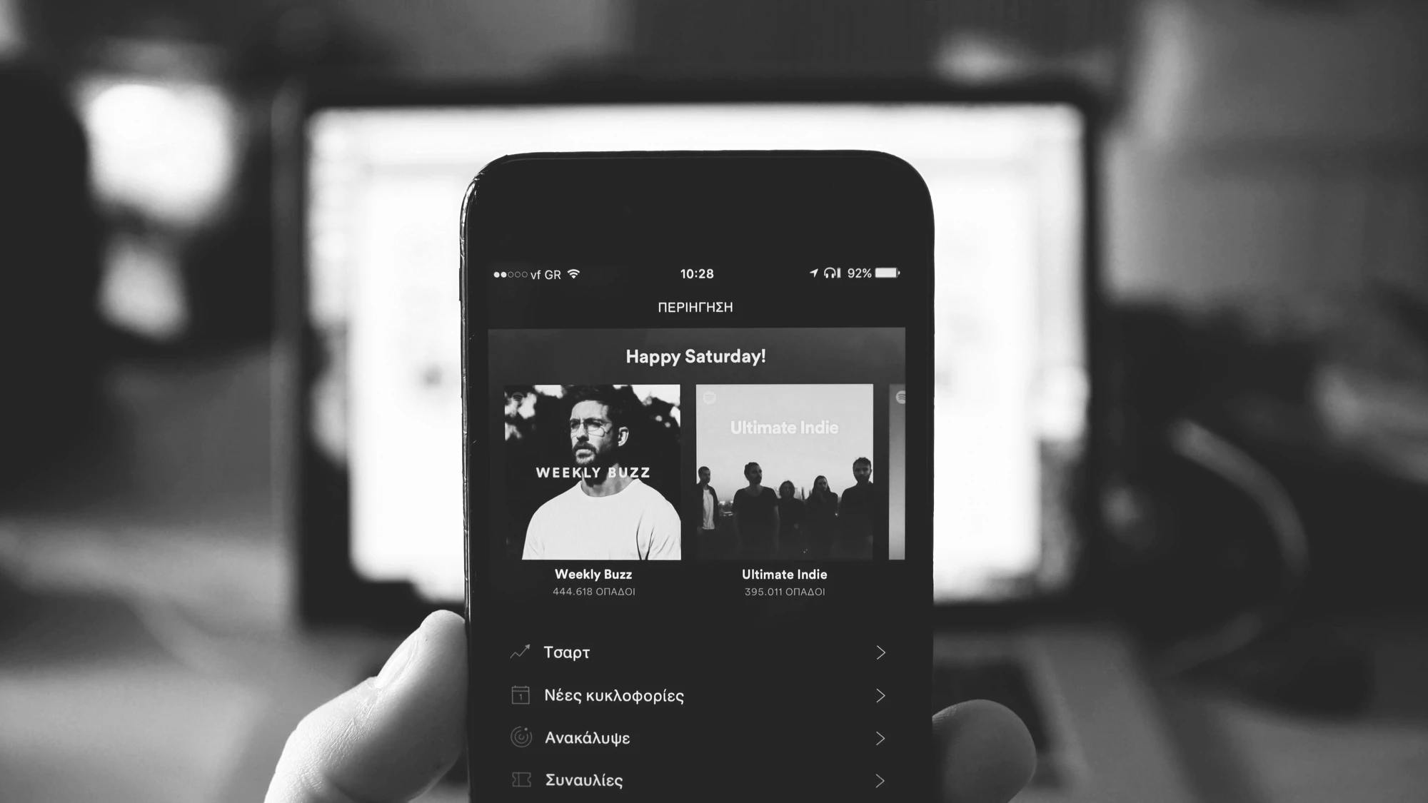 A person holds a phone in the middle of the screen with Spotify rendered on the screen. The 'Weekly Buzz' and 'Ultimate Indie' playlists button are prominent.